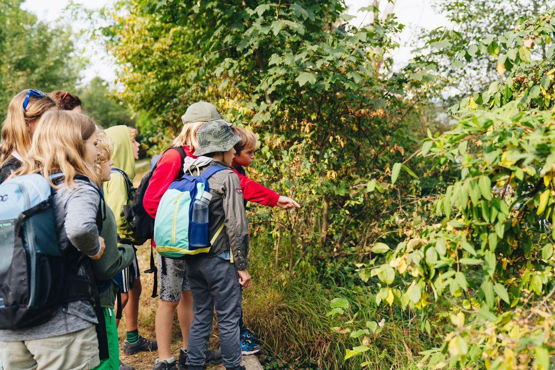 Kinder mit Rucksäcken vor Büschen