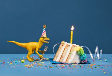 Gelber Kunststoffdinosaurier neben einem Stück Geburtstagstorte 