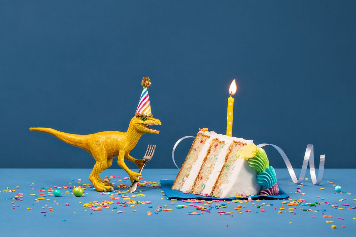 Gelber Kunststoffdinosaurier neben einem Stück Geburtstagstorte 